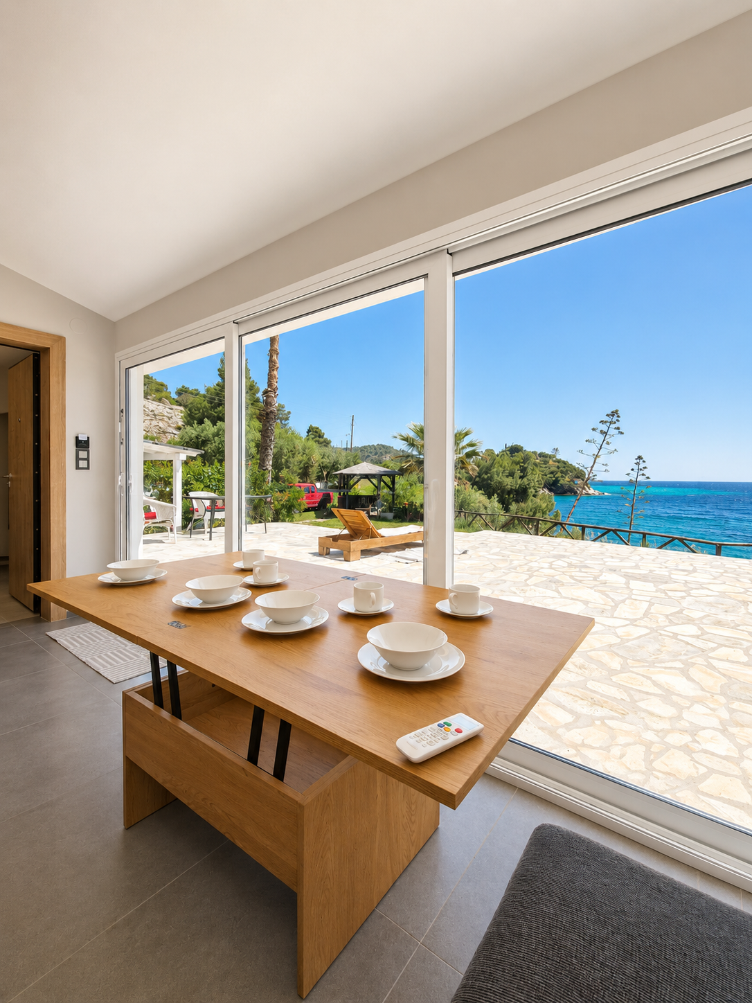 Dining table inside the studio looking through full-height glass to the sea and gazebo